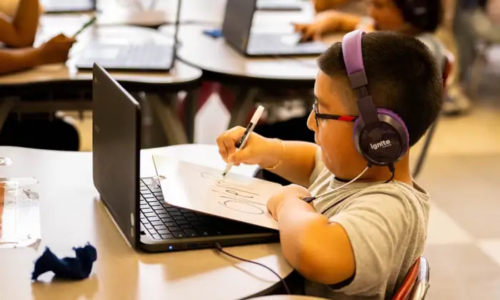 child wearing headphones works with virtual tutor on a laptop