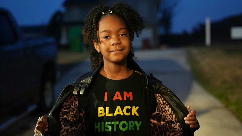 student holds open coat to reveal a shirt that reads I am Black history