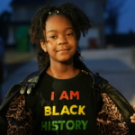 student holds open coat to reveal a shirt that reads I am Black history