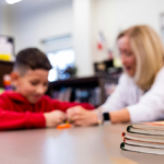 English Language Learner sits with teacher administering assessment in classroom
