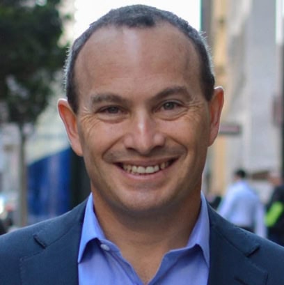 A close up photo of Evan Marwell's face shows him wearing a blue shirt and suit jacket