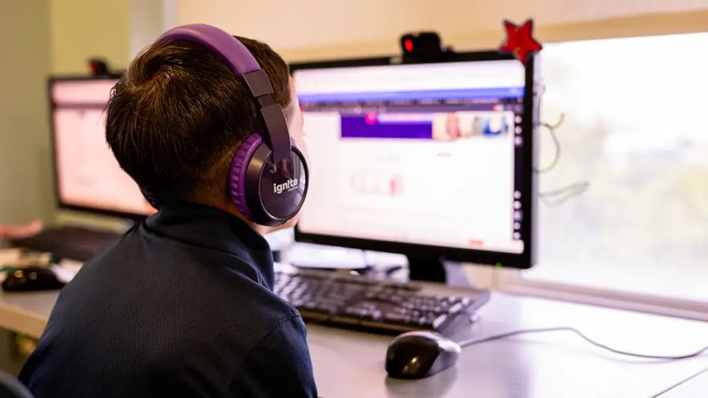 First Grade student wearing headphones talks to his virtual tutor while facing computer screen