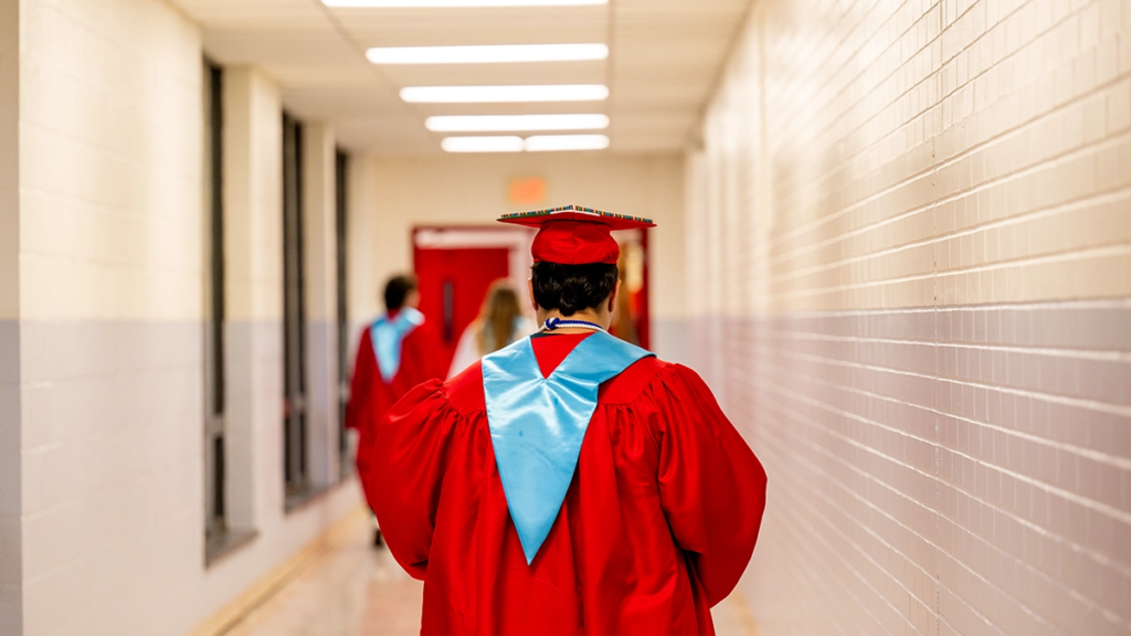 a high school graduate walks alone down a school hallway