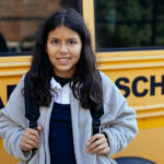 Multilingual Learner stands in front of a School Bus