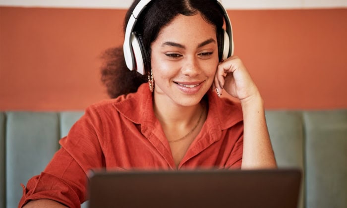 A Science Of Reading Tutor smiles at a student on a computer screen while wearing noise-canceling headphones