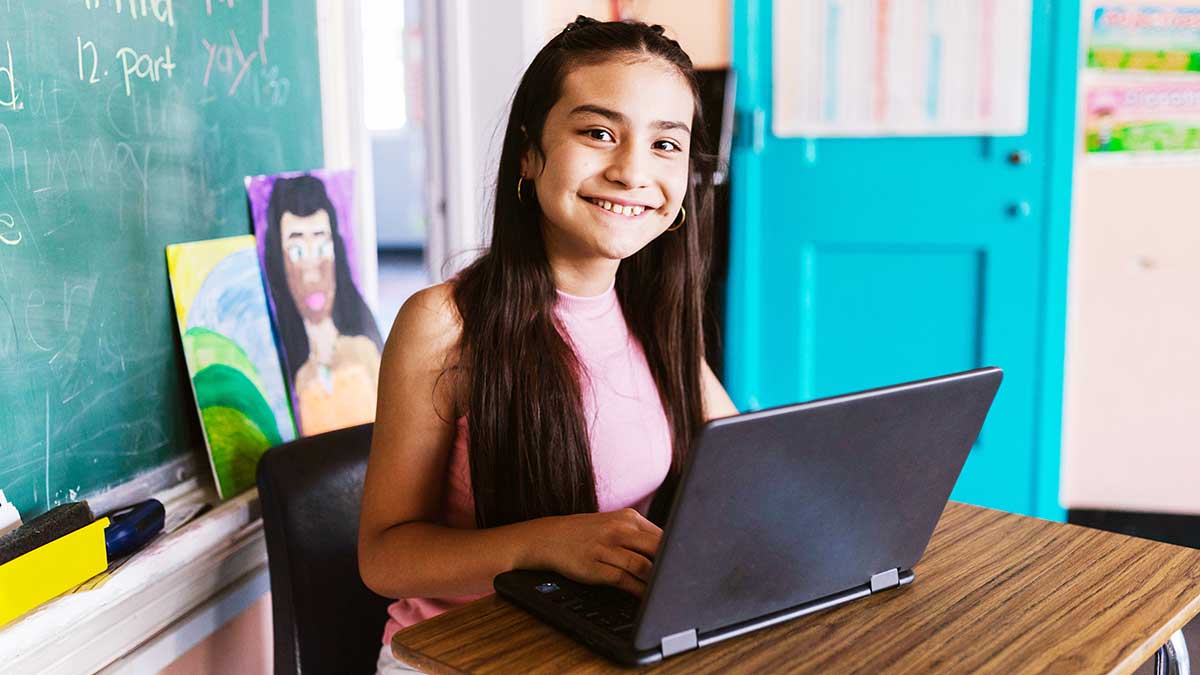 A female middle school student looks up from her laptop during an online tutoring session at school