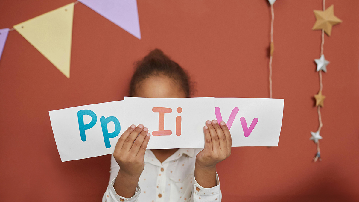 Student Learning Foundational Reading Skills holds up paper with the letters P, I and V