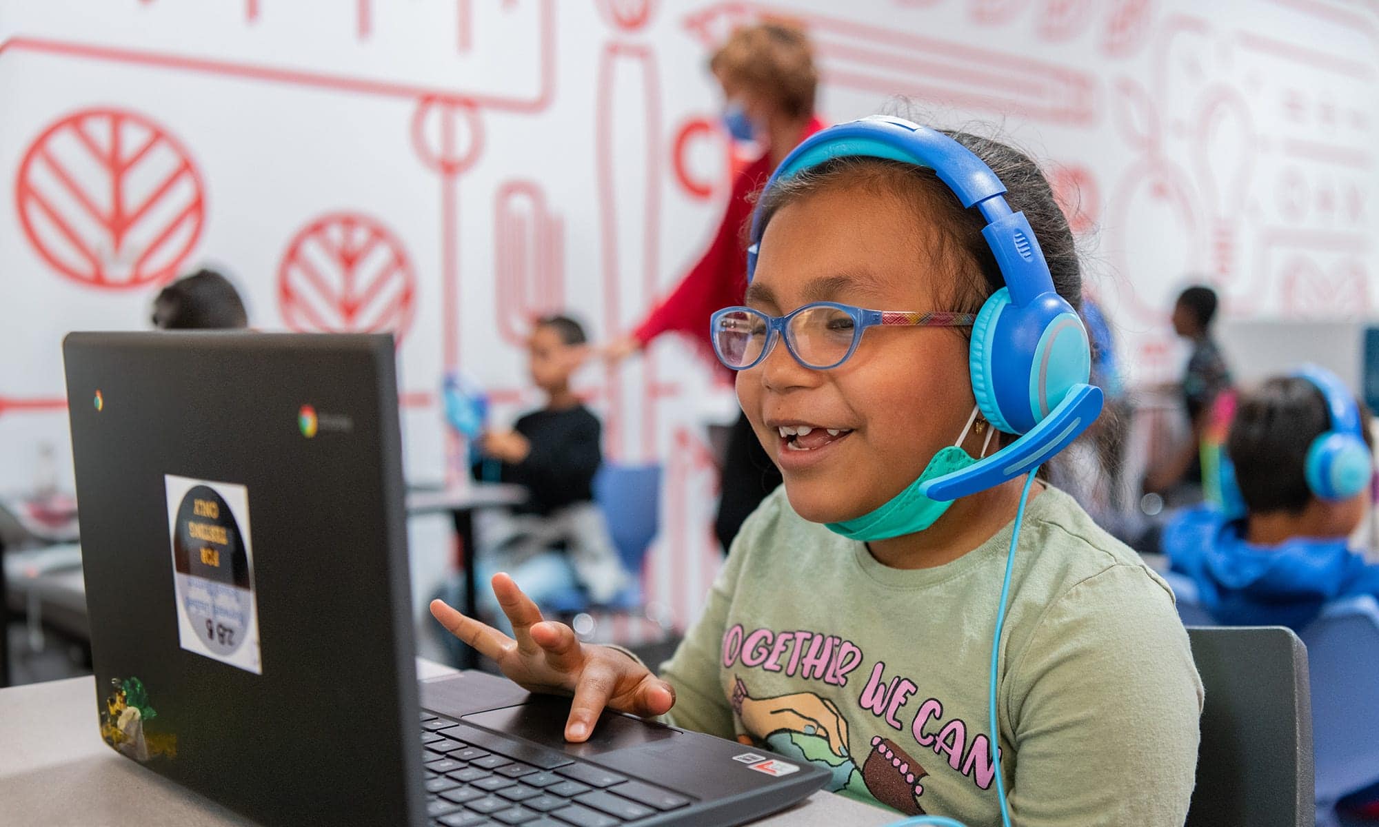 A 1st grade student wearing headphones smiles at her laptop during an online tutoring session