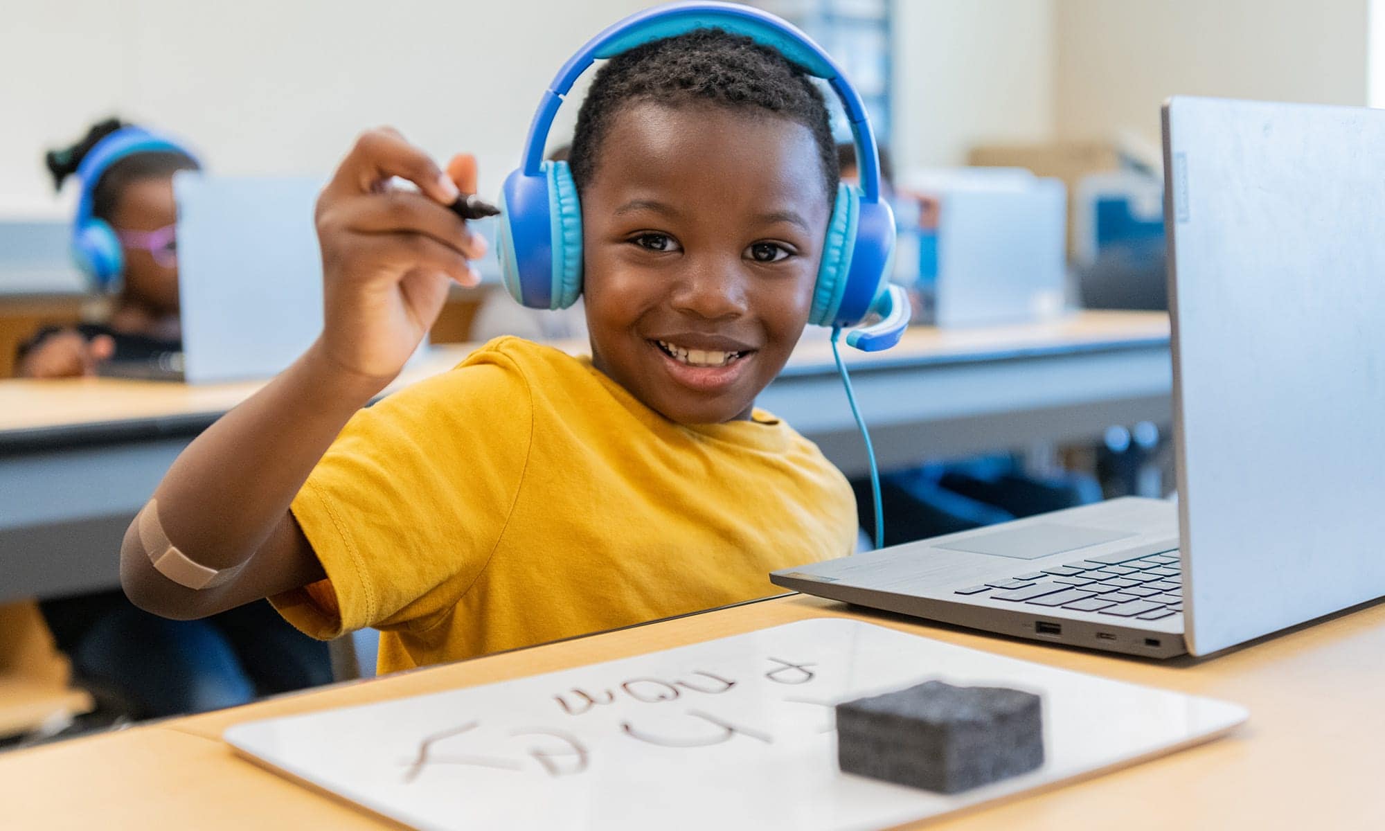 A 1st grade student holds a marker in the air while wearing headphones during his online tutoring session