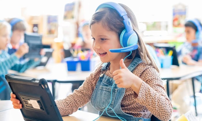 A student holds her tablet and gives a thumbs up to her virtual tutor