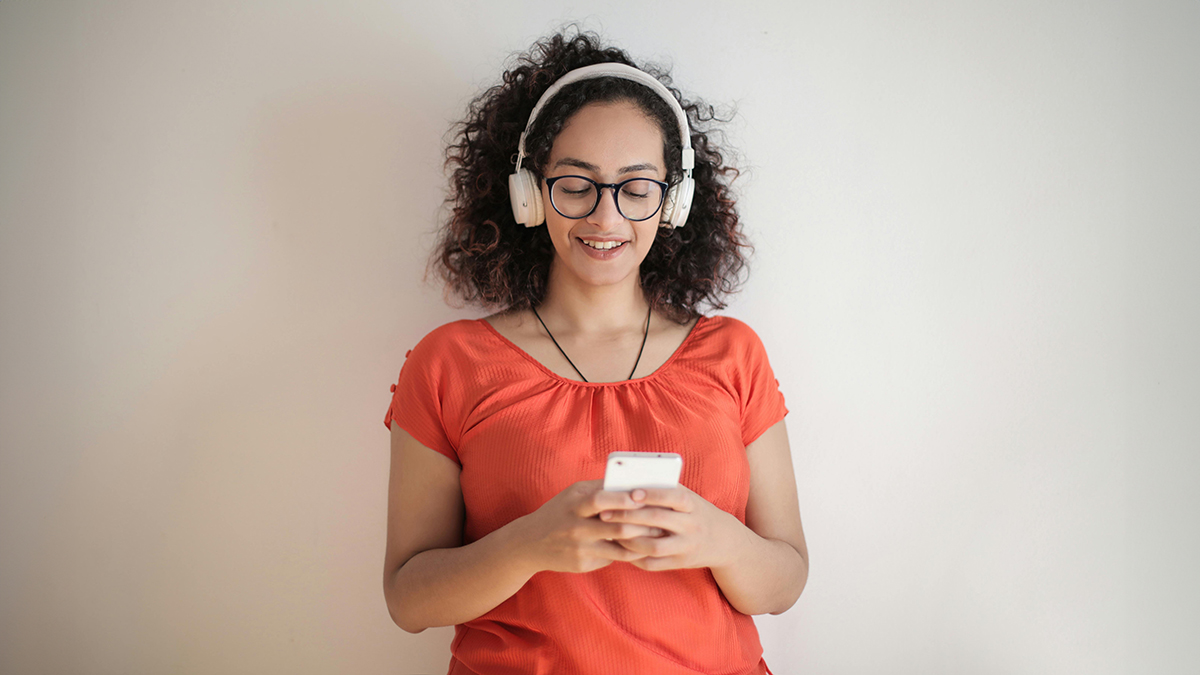 A female-presenting educator wearing headphones looks at her phone while listening to a science of reading podcast