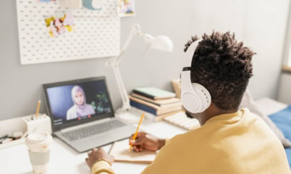 a tutor is seen from behind wearing headphones and working on a laptop