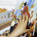 a child's hands turn the pages in a book during a whole language lesson