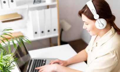 a female tutor works on a laptop while wearing headphones